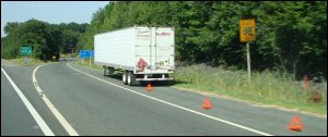 The trailer from a tractor-trailer combination, left on the shoulder of an off-ramp, with hazard triangles behind it.