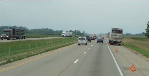 Big truck broken down on the side of the road with hazard triangles behind it.