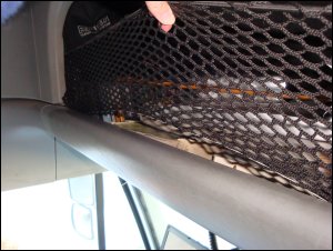 Vicki holds up the cargo net that stretches from side to side across the overhead storage compartment in Mike's truck to show how the bottom has come loose from the knobs, potentially allowing materials to fall out during travel.