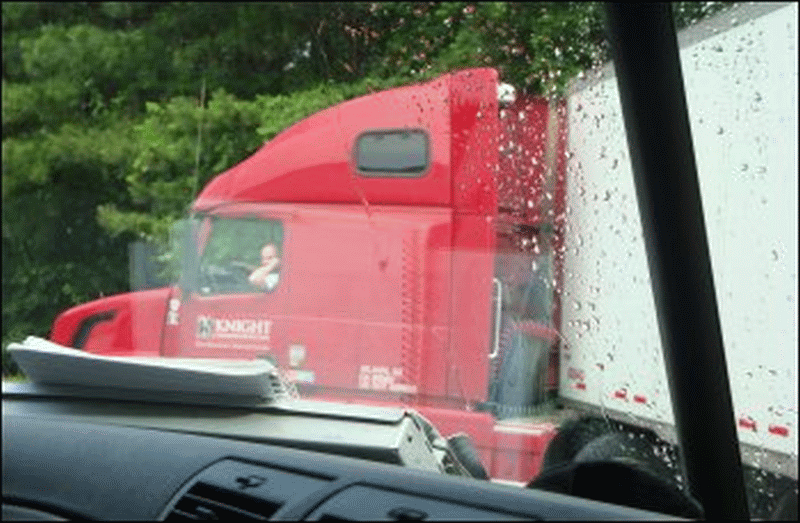 A professional truck driver backs into a dock while talking on his cell phone.