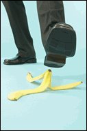 Man about to step on a banana peel dropped on the floor. If one steps on a slippery banana peel the wrong way, he will slip and fall.