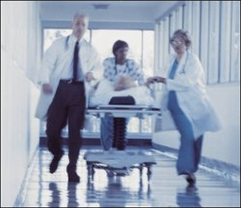 A patient is wheeled down a hospital corridor by health care professionals.