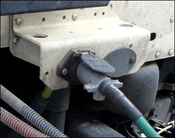 The electrical cord or pigtail that carries power from the tractor to the trailer, shown plugged into the socket on the back side of the tractor.