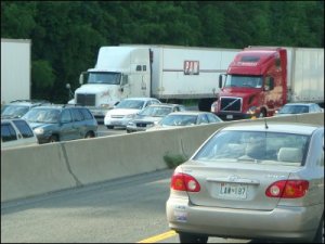 Following distance of big trucks on opposing side of the interstate in stalled traffic. The white truck in the outside lane is behind another big truck; the red truck in the middle lane is behind a car.