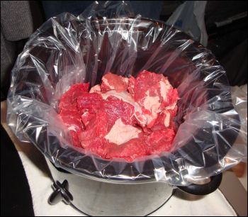 Beef stew chunks of meat in a slow cooker liner in the bottom of a crock pot.