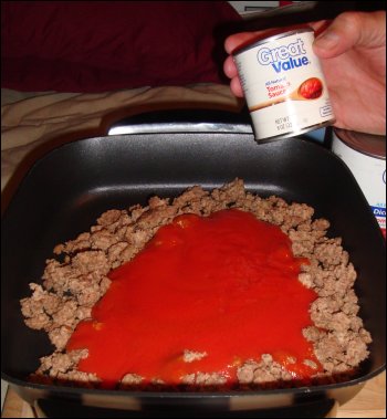 Tomato sauce is added to the electric skillet on top of the ground beef.