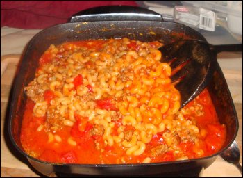 Stirring the macaroni and tomato sauce mixture partway through the cooking cycle.