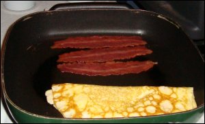 Three slices of previously cooked turkey bacon are reheated to eat with scrambled eggs.