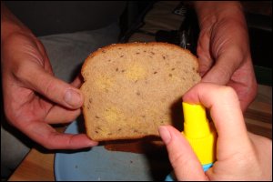 While Mike holds the bread for a grilled cheese sandwich, Vicki sprays it with spray butter. This slice will go butter side down directly on the electric skillet.