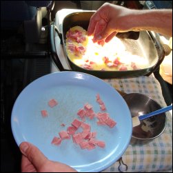 Sprinkling ham chunks on egg mixture in a heated electric skillet for a ham and cheese omelette.