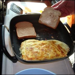 Placing buttered bread, butter side down, in heated electric skillet beside flipped ham and cheese omelette.