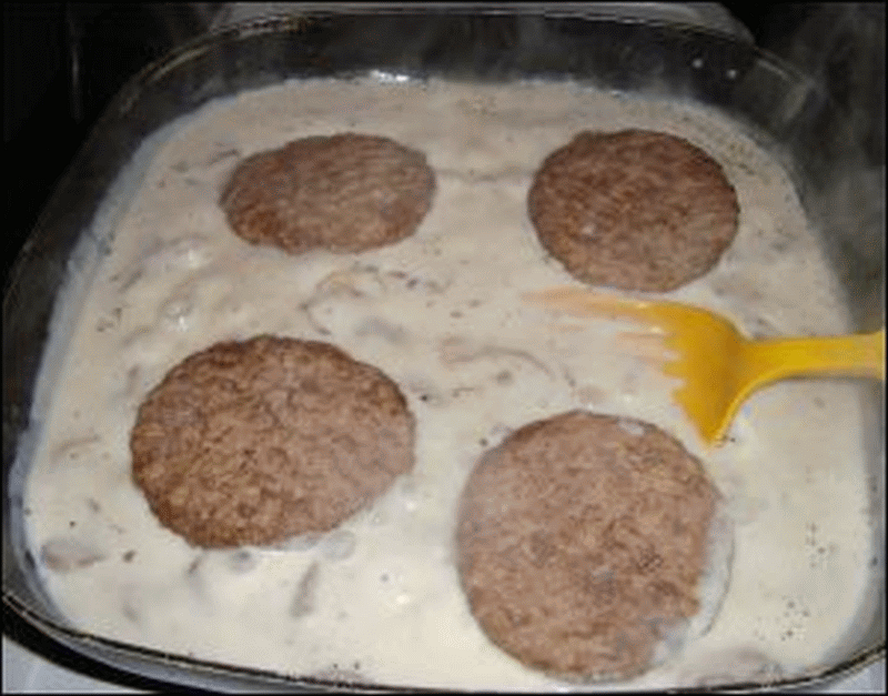 Hamburger steak with mushroom gravy being prepared in an electric skillet.