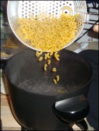 Pouring dry macaroni elbows from the fryer/steamer basket into a Presto Kitchen Kettle, to make macaroni and cheese.