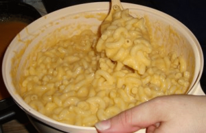 Stirring the cheese sauce into the cooked pasta for macaroni and cheese.