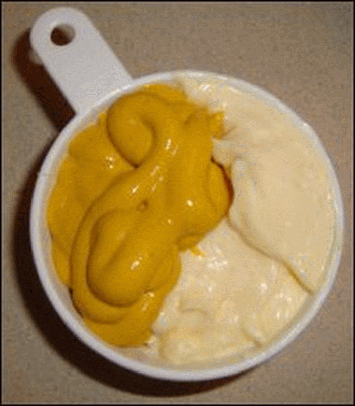 A 3/4 cup measuring cup with half each of mayonnaise and prepared mustard.