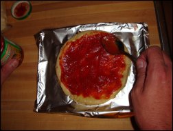 Preparing the homemade pizza by spreading on the pizza sauce.