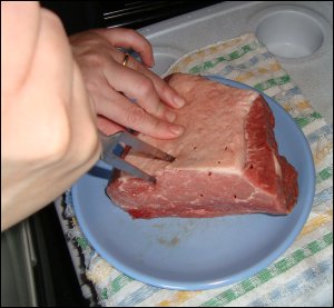 Vicki prepares the pot roast by poking it with a large fork, so that the bouillon mixture can work into the interior of the meat.