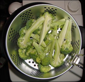 Steaming broccoli in the basket of a hot pot above boiling water.