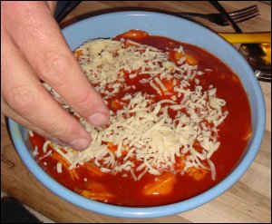 Professional driver Mike Simons sprinkles shredded mozzarella cheese on top of the heated ravioli.