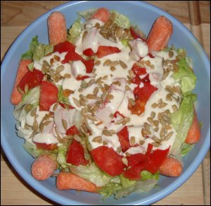 A salad of iceberg lettuce, tomatoes, baby carrots, ranch salad dressing and sunflower kernels.