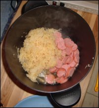 A smoked sausage cut up with sauerkraut in a hot pot, ready to be heated up.