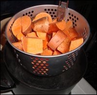 Cleaned and diced sweet potatoes in a fryer/steamer basket resting on the edge of a hot pot just before being put down into boiling water.
