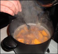 Mike tests the doneness of the sweet potatoes with a fork, being careful not to get burned by the steam from the boiling water in the hot pot.