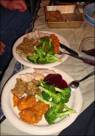 Thanksgiving dinner is served! Both plates show a serving of turkey, bread dressing, sweet potato casserole and steamed broccoli. The plate in the foreground also shows jellied cranberry sauce. You can see the edge of the bowl with whole berry cranberry sauce on the right and the pan containing the remainder of the bread dressing in the background.