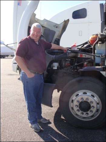 Mike stands by his truck, hood up, pointing to a turkey in its package, sitting in a pan on top of the engine, as though he were going to use the engine's heat to cook it.