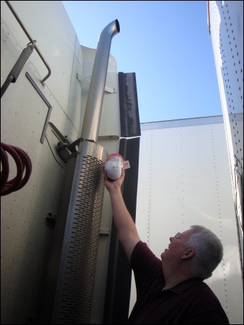 Mike holds a boneless turkey still in the packaging up to the exhaust stack on the back of the tractor he drives for his trucking company, as if he were going to use this method for cooking turkey.