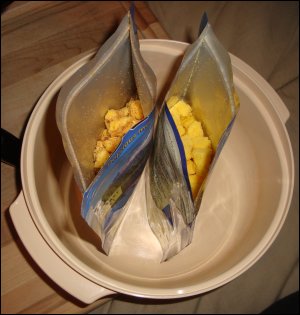 Both pouches of Mountain House Freeze Dried Scrambled Eggs with Bacon are standing upright in a large bowl, waiting for boiling water to be added.