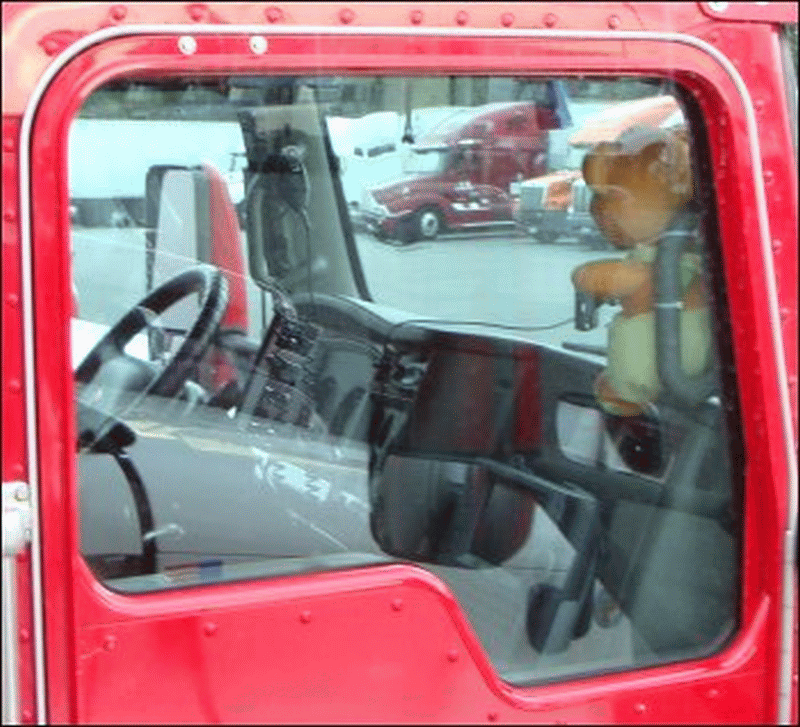 A stuffed animal is strapped to a handle on the passenger side of a large truck.