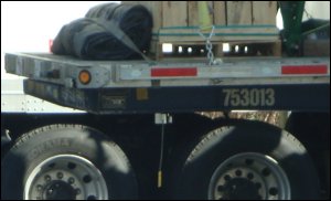 A king pin lock is installed under a dropped flatbed trailer.