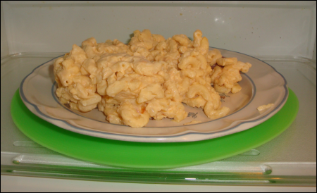 A lime green Micro Easy Grab silicone disk under a plate of macaroni and cheese in the microwave oven.