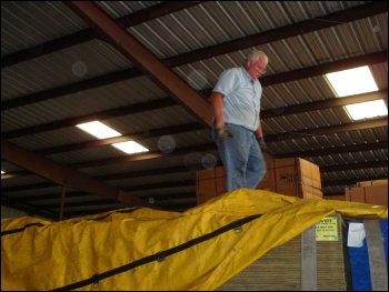 Professional truck driver Mike Simons is on top of a load on top of his trailer, in the process of adjusting his tarp.