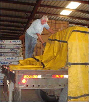 Professional truck driver Mike Simons is on top of his trailer, adjusting his tarp.