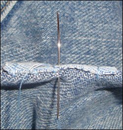 A close-up of holding the jeans material on a fold to more easily sew the patch with preliminary stitches more firmly in place.