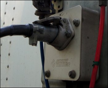 The electrical cord or pigtail that carries power from the tractor to the trailer, shown plugged into the socket on the trailer.