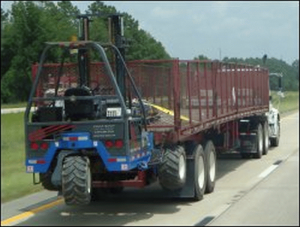 A daycab tractor pulls a flatbed trailer with side rails and a forklift.