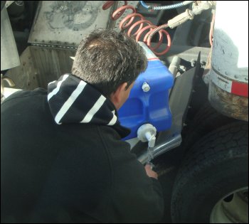 This driver is dispensing water from a 5-gallon water container that is balanced near the catwalk behind his tractor.