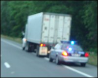 A large truck pulled over on the shoulder by a police officer.