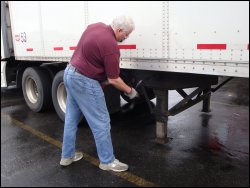 Mike Simons is lowering the landing gear on a trailer that he is preparing to drop in a truck stop parking lot.