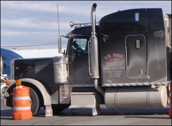 A black Peterbilt tractor covered in road dirt and road salt, badly in need of a truck wash.