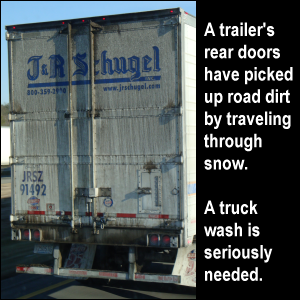 A trailer's rear doors have picked up road dirt by traveling through snow. A truck wash is seriously needed.