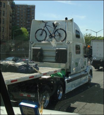 A trucker bike on the back of a semi tractor hauling a flatbed trailer.